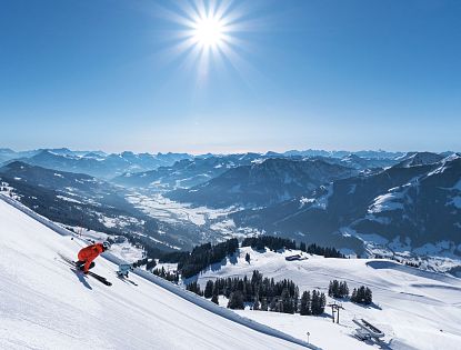 Zwei Skifahrer auf schwarzer Piste auf Südabfahrt von Gipfel Hohe Salve mit Blick über Brixental bei Sonnenschein in SkiWelt Brixen