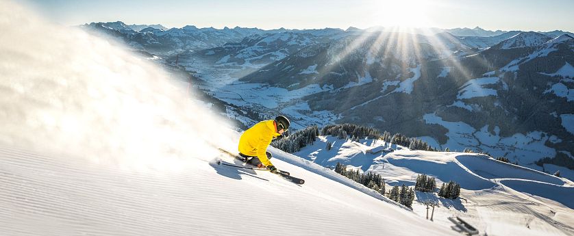 Zwei Skifahrer auf schwarzer Piste Südabfahrt von Gipfel Hoher Salve bei Sonnenaufgang in SkiWelt Brixen mit Blick auf Brixental