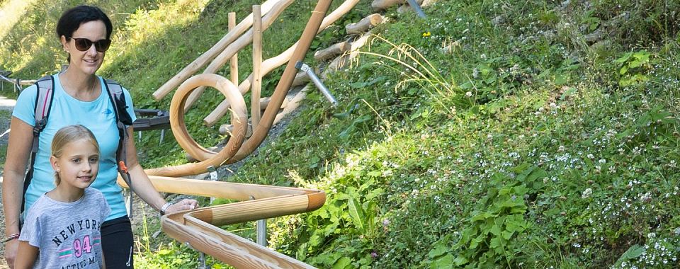 Een vrouw en een kind wandelen langs een houten parcours in een groene omgeving.
