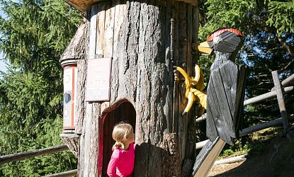 Child in pink shirt looks at banana decoration on rustic wooden playhouse.