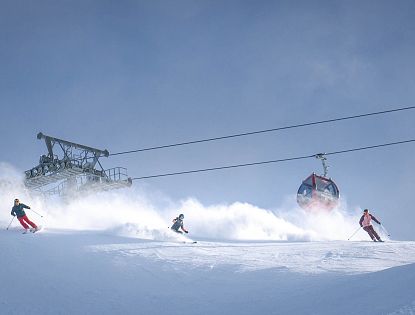 A skier descends a snowy slope under a clear blue sky beside a gondola lift transporting passengers uphill.