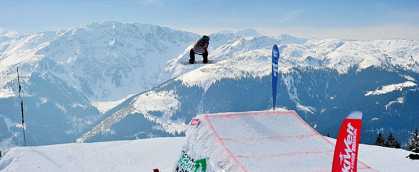 Snowboarder in de lucht boven een sneeuwhalfpipe met besneeuwde bergen en een blauwe lucht op de achtergrond, sportsfeer en adrenaline. Berglandschap.