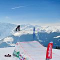Snowboarder in de lucht boven een sneeuwhalfpipe met besneeuwde bergen en een blauwe lucht op de achtergrond, sportsfeer en adrenaline. Berglandschap.