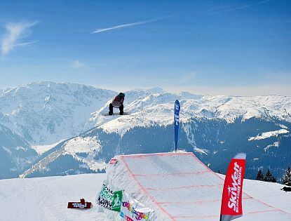 Snowboarder in de lucht boven een sneeuwhalfpipe met besneeuwde bergen en een blauwe lucht op de achtergrond, sportsfeer en adrenaline. Berglandschap.