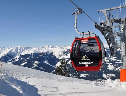 A red gondola labeled 'Westendorf Choralpe' against snowy mountain peaks and blue sky.