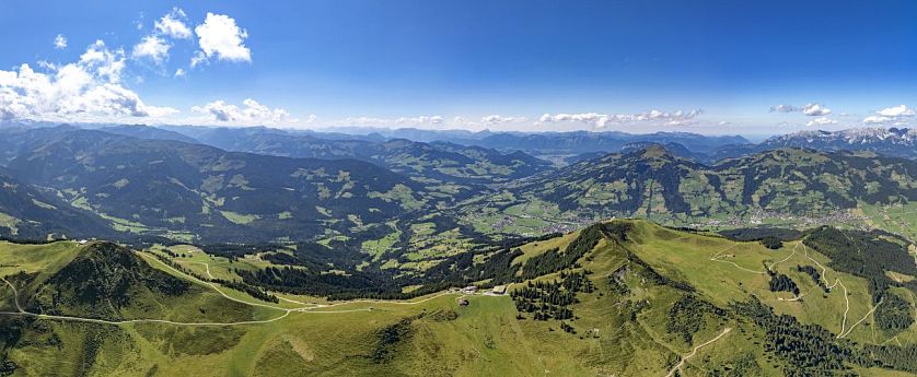 Panoramic view of green mountains and blue sky, with rolling hills and paths.