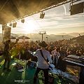 Band speelt op buitenpodium in de bergen bij zonsondergang, omringd door groot publiek en bergachtergrond.