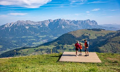 Eine Familie genießt eine Berglandschaft mit grünen Wiesen und Rückansicht einer beeindruckenden Bergkette im Hintergrund bei klarem Wetter.